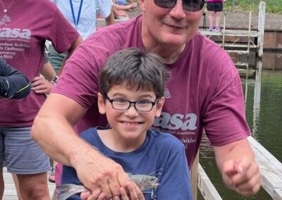 A smiling child holds a fish with a volunteer's help