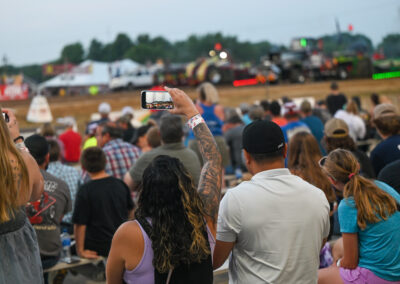 Women taking a selfie in the crowd at the Tomah Tractor Pull, smiling and enjoying the event atmosphere.