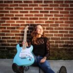 Payton Eilers sitting on the floor with a blue guitar