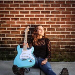 Payton Eilers sitting on the floor with a blue guitar
