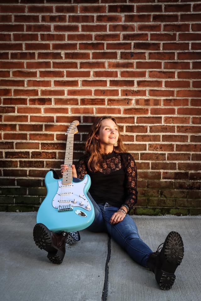 Payton Eilers sitting on the floor with a blue guitar