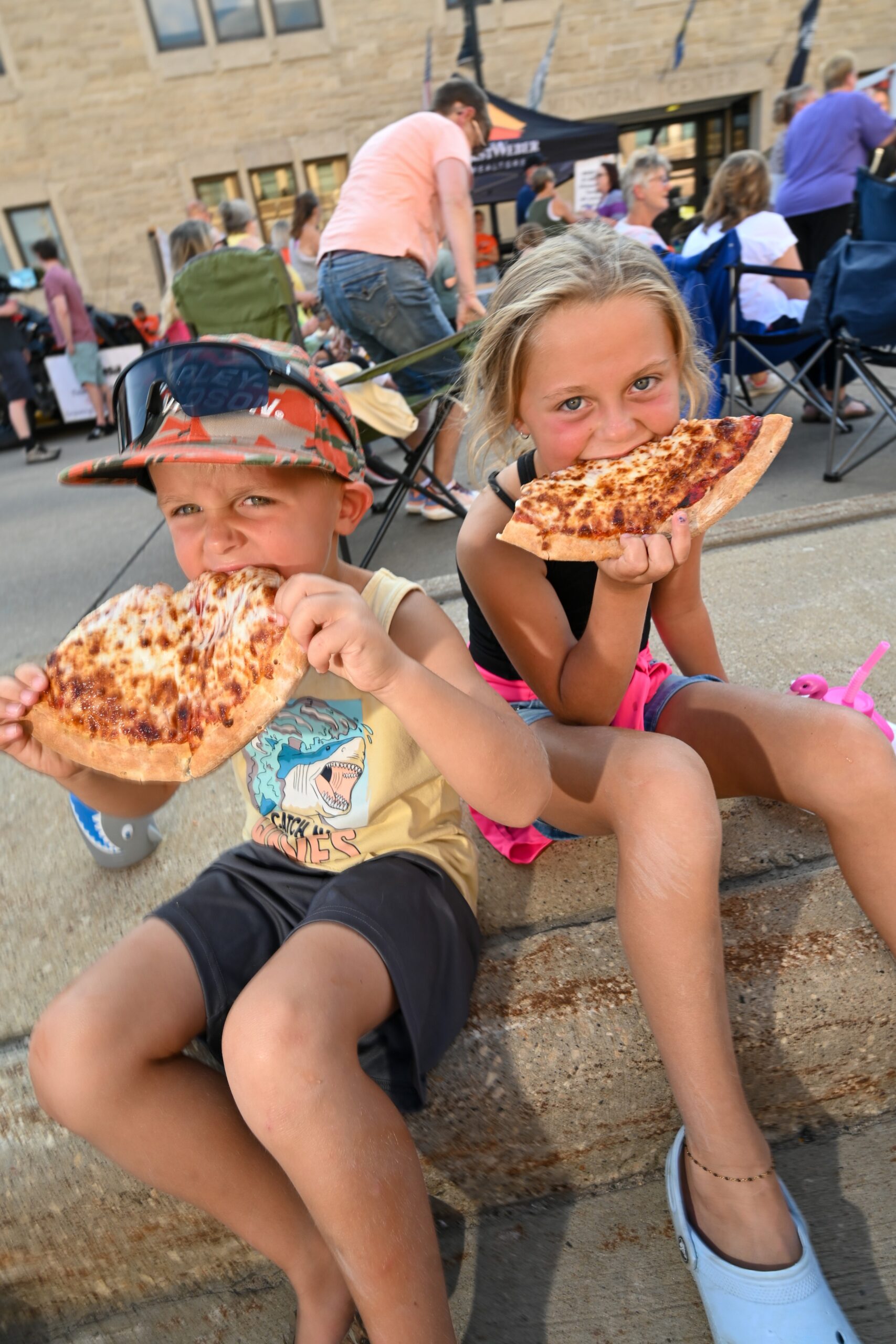 kids with pizza Two children eat pizza while sitting on a curb.