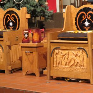 Two throne like chairs made from wood sit next to each other, with a table in the middle of them, two mugs sit on top of the table.