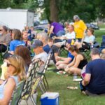 A photo of people sitting in lawn chairs while some sit on the ground.