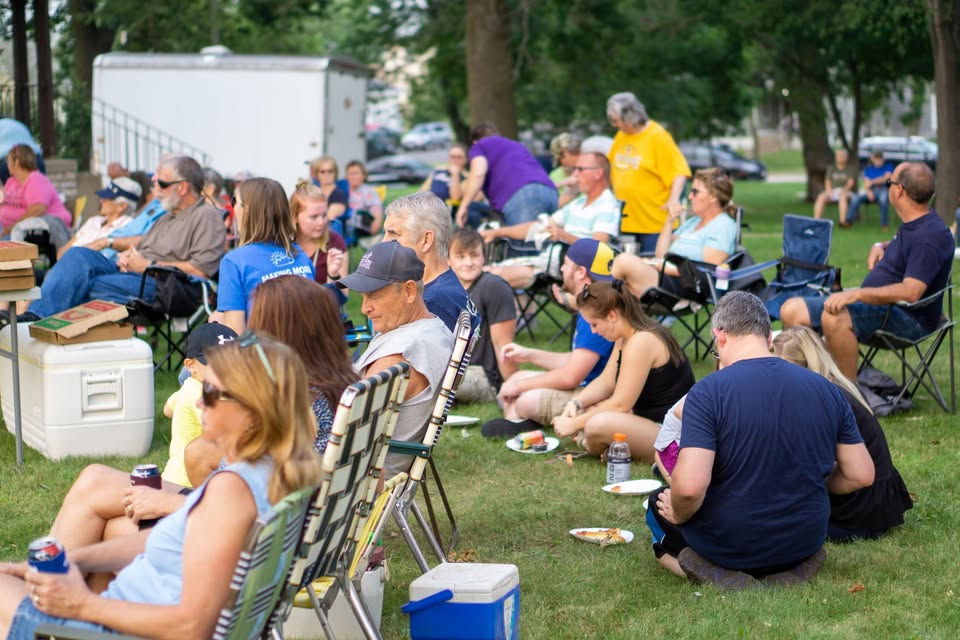 A photo of people sitting in lawn chairs while some sit on the ground.