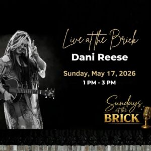 A photo of Dani Reese holding a guitar and the peace sign.