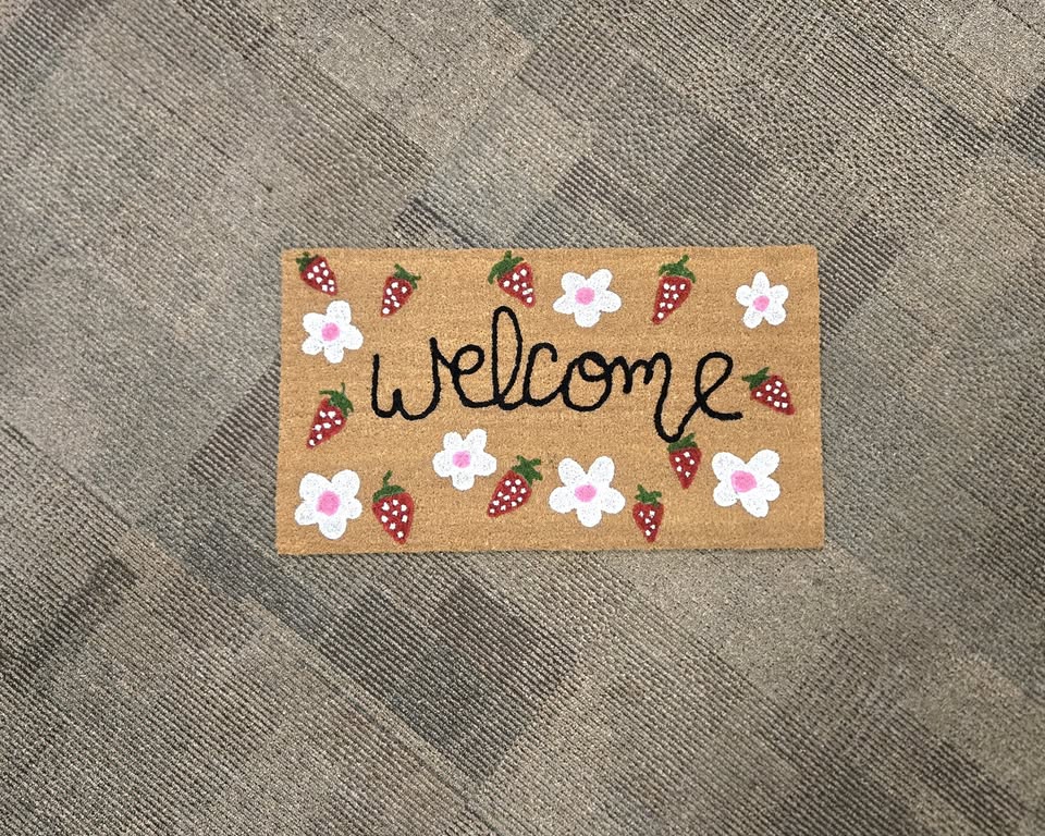 A welcome mat painted with flowers and strawberries