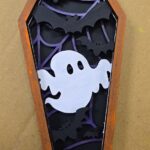 a layered wood craft project of a coffin with a cute ghost