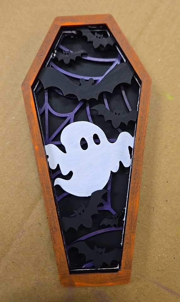 a layered wood craft project of a coffin with a cute ghost