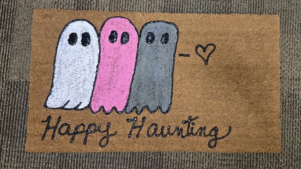 A doormat with three ghosts painted on it and the words "Happy Haunting"